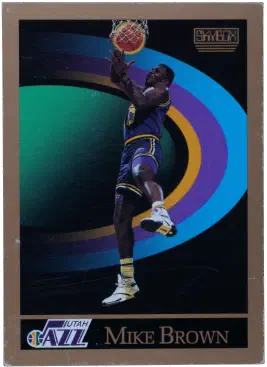 The front of a 1990 SkyBox basketball card featuring Mike Brown of the Utah Jazz. The photo shows Mike jumping up to catch the ball that has gone through the hoop against a computer generated background which evokes the planet Saturn.